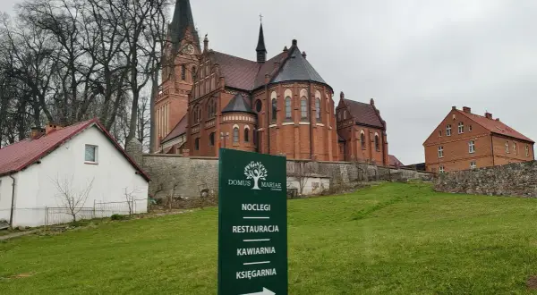 Dom Pielgrzyma w Gietrzwałdzie oferuje noclegi, restaurację, kawiarnię i księgarnię. W tle kościół.
