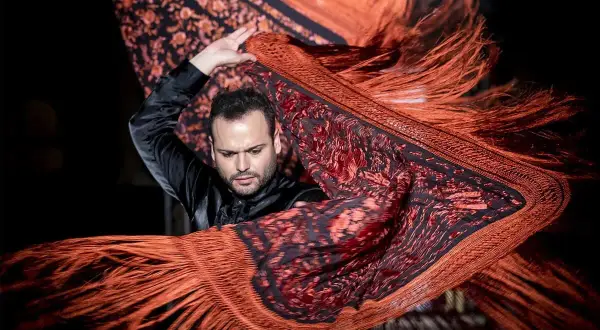 Un bailarín flamenco agita un mantón de Manila de origen oriental, con flecos anaranjados y estampado floral.