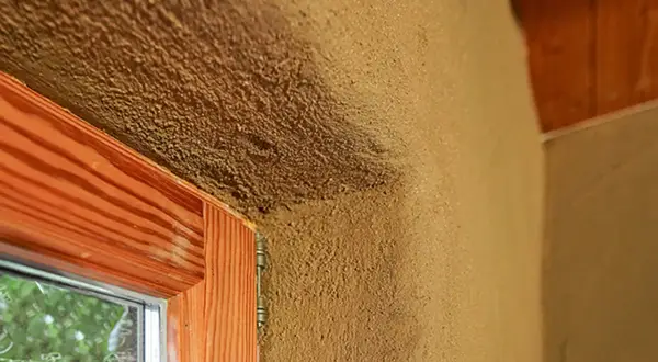 Lehmputz nachteile: raue Textur, die Schmutz anziehen kann, um ein Fenster mit Holzzarge und sichtbarem Putz.