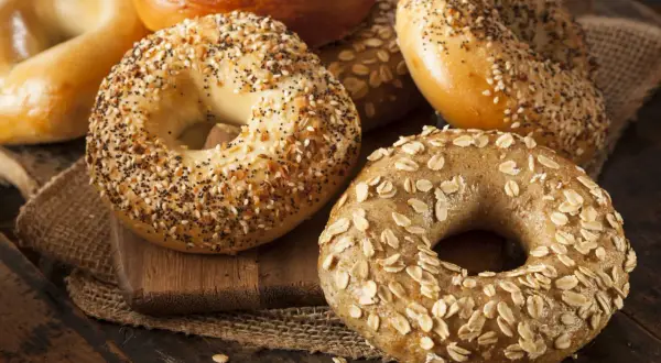 Un assortiment de bagels chauds, certains garnis de graines de sésame et de pavot, d'autres d'avoine, sur une planche en bois.