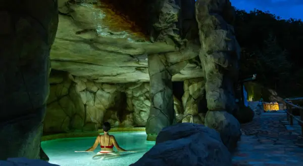 Una mujer disfruta de un relajante spa de noche en una piscina natural rodeada de rocas.