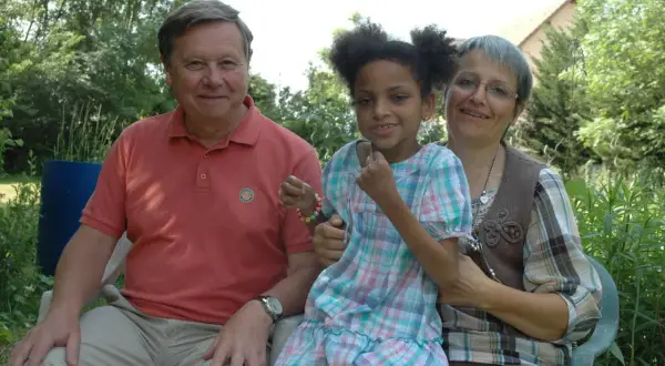 Un homme, une femme et une petite fille souriants, peut-être la famille de Leonard Berducat, profitent d'un moment ensoleillé dans un jardin.