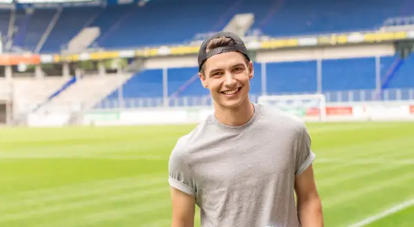 Junger Mann mit Kappe und Buch im Stadion, bereit für seinen Eventmanagement Master.