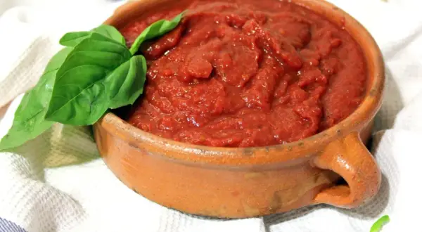 Un cuenco de barro rústico lleno de vibrante salsa de tomate casera, adornado con una hoja de albahaca fresca.