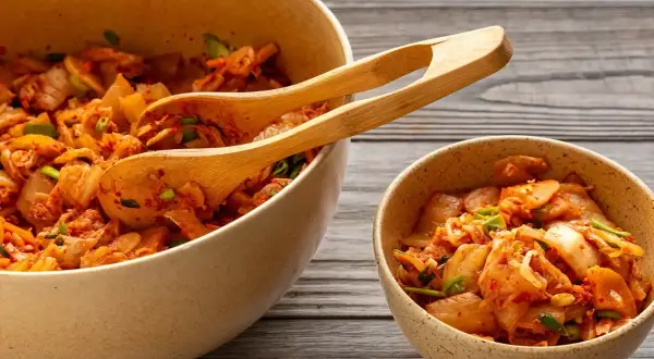 Två skålar med kryddig, fermenterad mat, troligen kimchi, med träskedar i den större skålen.
