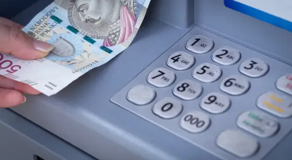 Dłoń wkłada banknot 500 zł do bankomatu. Zastanawiasz się, mbank ile idzie przelew?