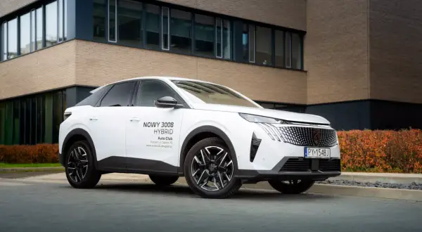 Biały Peugeot 3008 Hybrid, nowoczesny plug in, zaparkowany przed budynkiem z ceglaną fasadą.
