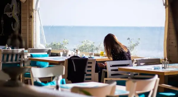 Kobieta siedzi przy stoliku w restauracji z widokiem na morze. Idealne miejsce, gdzie zjeść we Władysławowie.