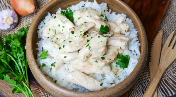 Schmackhaftes Puten Geschnetzeltes in cremiger Sauce auf Reis, garniert mit Petersilie. Daneben Zwiebel und Knoblauch.