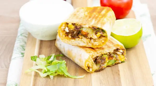 Pyszny burrito przepis: dwa połówki burrito z ryżem, mięsem mielonym, kukurydzą i warzywami, podane z limonką i śmietaną.