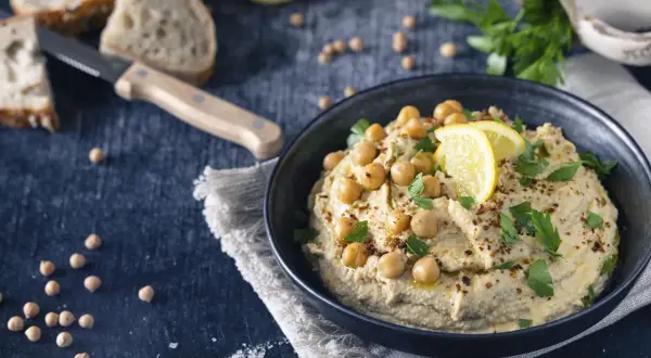 Cremiger Hummus, garniert mit Kichererbsen, Zitrone und Petersilie. Ein köstliches Hummus Rezept Original, bereit zum Dippen mit Brot.