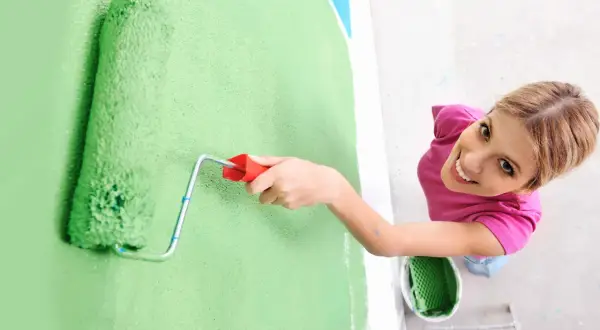 Frauen streichen bei Auszug nach 5 Jahren die Wand grün. Sie lächelt fröhlich, während sie mit der Rolle die Farbe aufträgt.