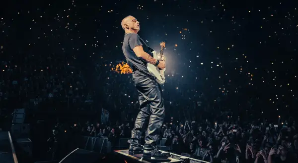 Eros Ramazzotti gra na gitarze podczas koncertu, a tłum w ciemnościach trzyma zapalone telefony.