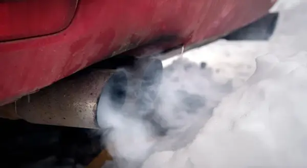 Roter Auspuff mit Rauch im Schnee. Der Motor läuft, um das Auto im Winter warm zu halten.