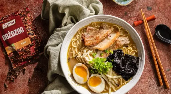 Jak zrobić ramen? Aromatyczny bulion, makaron, jajko na pół, chrupiąca wieprzowina i nori. Obok paczka goździków Prymat.