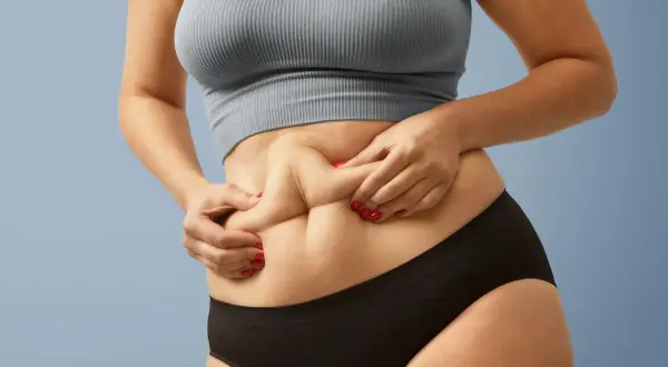 Dłonie chwytają fałdy skóry na brzuchu, ukazując sylwetkę skinny fat.