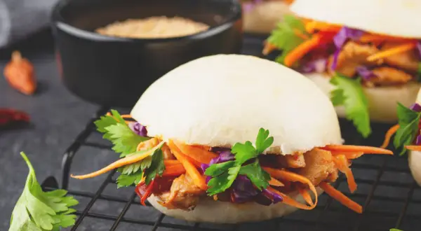 Saftiger bao burger mit Hähnchen, Karotten, Rotkohl und Koriander auf einem Rost.