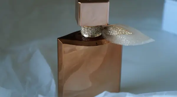 Elegancka butelka perfum Lancome Eclat w kolorze miedzi, ozdobiona brokatową wstążką, otulona delikatnym białym papierem.