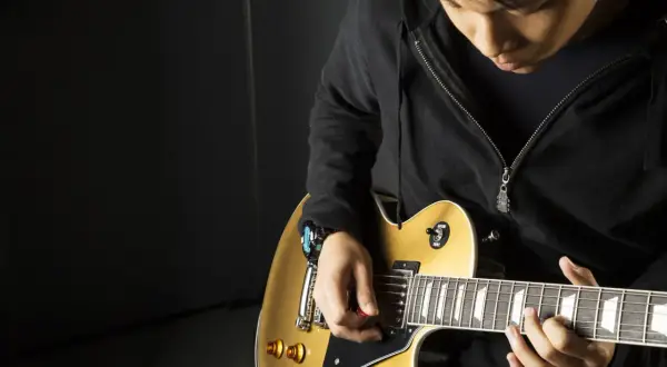 Młody gitarzysta z kostką w dłoni pokazuje, jak trzymać kostkę od gitary, grając na złotej gitarze elektrycznej.
