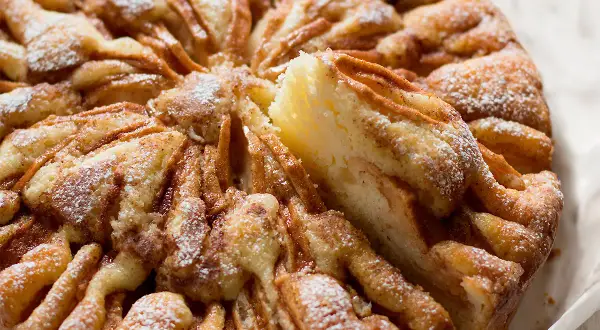 Una deliziosa torta di mele, cosparsa di zucchero a velo, con una fetta sollevata che rivela la morbida consistenza.