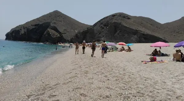 Gente disfrutando del sol y el mar en la playa de los Muertos en Carboneras, con sus icónicas montañas de fondo.