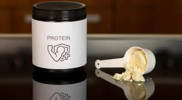Barattolo di proteine in polvere e misurino con polvere. Le proteine sono fondamentali per la costruzione muscolare.