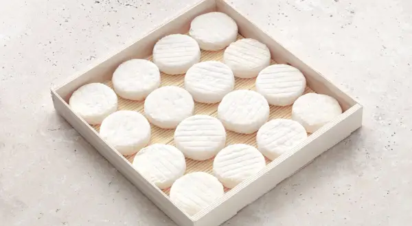 Un plateau en bois présente une rangée de petits fromages ronds, évoquant l'origine du saint marcellin fromage.