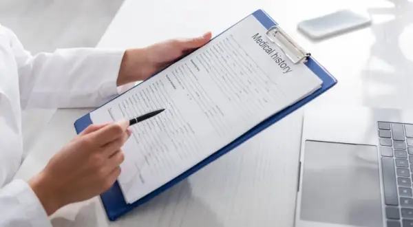 Manos de médico revisan un historial médico en un portapapeles, preparándose para un certificado médico A2.