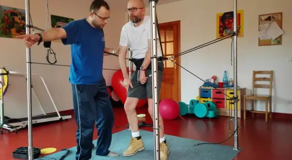 Fizjoterapeuta pomaga pacjentowi ćwiczyć z użyciem sprzętu do rehabilitacji po udarze mózgu.