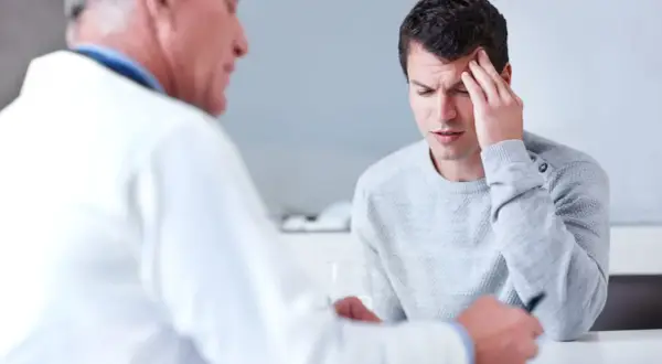 Ein Mann mit Kopfschmerzen spricht mit einem Arzt. Die Diagnose: ein gutartiger hirntumor.