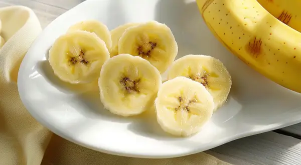Fette di banana su un piatto bianco, con banane intere sullo sfondo. La banana è astringente o lassativa, a seconda della maturazione.