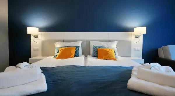 Przytulna sypialnia z dwoma łóżkami, pomarańczowymi poduszkami i białymi szlafrokami. Idealne miejsce na relaks, jak sugerują hotel hel opinie.