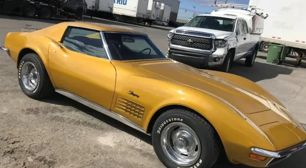 Złoty Chevrolet Corvette Stingray, klasyk wśród amerykańskich samochodów, stoi obok białej ciężarówki.