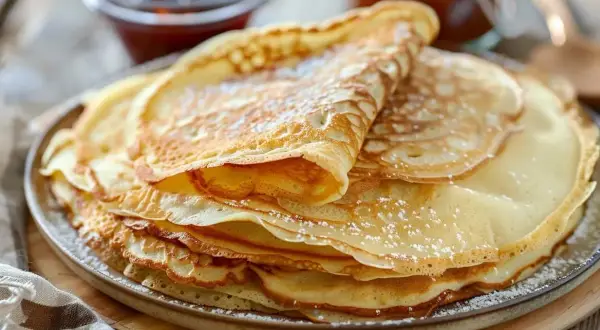 En hög med gyllene pannkakor, pudrade med florsocker. Perfekt för ett enkelt pannkakor recept.