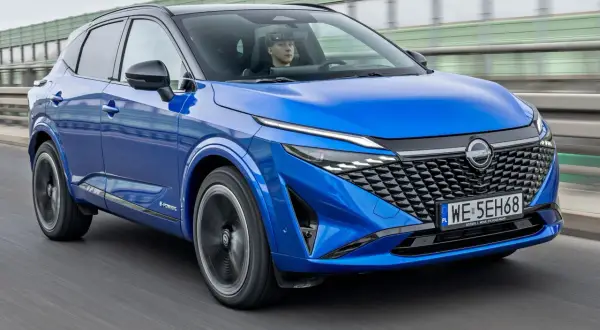 Niebieski Nissan Qashqai z kierowcą za kierownicą jedzie po drodze.