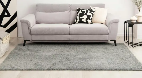 Grauer Hochflorteppich vor einem Sofa. So reinigen Sie Ihren langflorigen Teppich für ein frisches Zuhause.