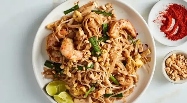 Pyszny sos pad thai z krewetkami, orzeszkami ziemnymi i limonką. Obok miseczka z chili i orzeszkami.