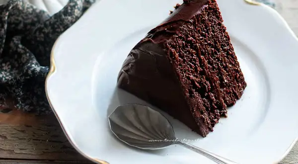 Una fetta di torta al cioccolato, ricca e umida, su un piatto bianco con un cucchiaino d'argento.
