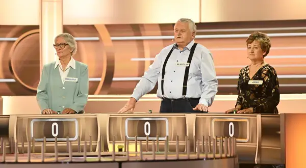 Trzech uczestników programu "Koło Fortuny" - Marianna, Władysław i Anna - stoi przy swoich stanowiskach.