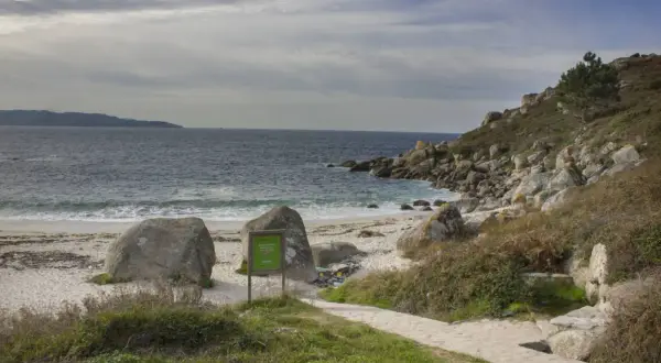 La playa de ancoradouro, con su arena blanca, rocas imponentes y el mar azul, invita a la contemplación. Un sendero de piedra serpentea hacia la costa.