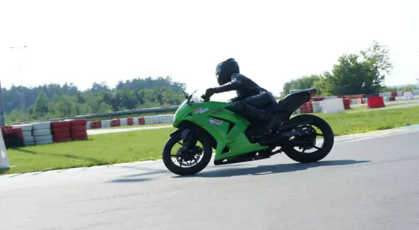 Motocyklista w kombinezonie na zielonym motocyklu ściga się na torze wyścigowym.