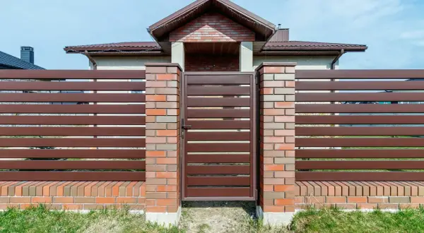 Eleganckie ogrodzenie z klinkieru i brązowych paneli, z solidną bramą wjazdową, stanowi ozdobę posesji.