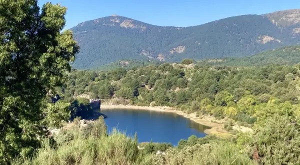 El embalse de Navalmedio, rodeado de bosques y montañas, refleja el cielo azul.