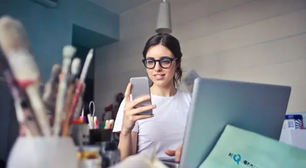 Kobieta z okularami przegląda coś na telefonie, obok laptop i pędzle. Czy to może być związane z tym, co to jitter?