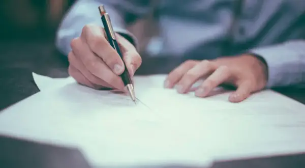 Dłoń pisze na papierze, być może notując, jak sprawdzić numer księgi wieczystej.