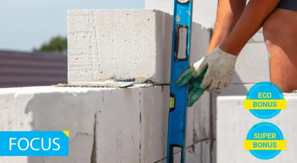Costruzione con blocchi di calcestruzzo aerato autoclavato, livella in mano per un lavoro preciso. Eco e Super Bonus in evidenza.