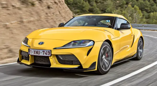 Żółta Toyota Supra pędzi po krętej drodze. Sprawdź aktualną toyota supra cena i poczuj moc!