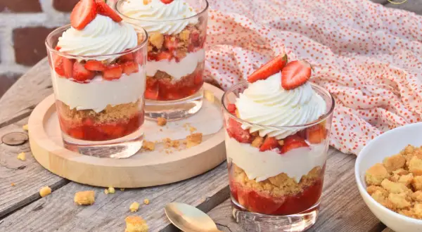Trois verrines fraise mascarpone facile, garnies de crème fouettée et de fraises fraîches, sur une table en bois.