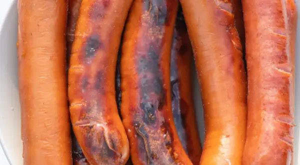 Zbliżenie na kilka grillowanych kiełbasek, niektóre lekko przypalone.