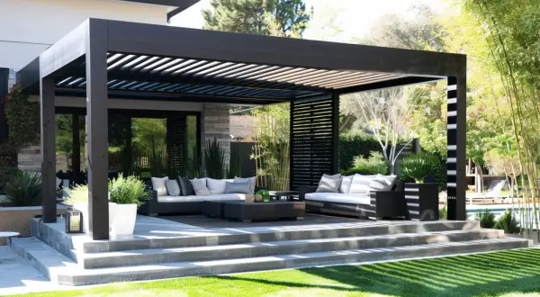 Nowoczesna, czarna pergola przed wejściem do domu, z wygodnymi sofami i stolikami, tworzy idealne miejsce do relaksu na świeżym powietrzu.